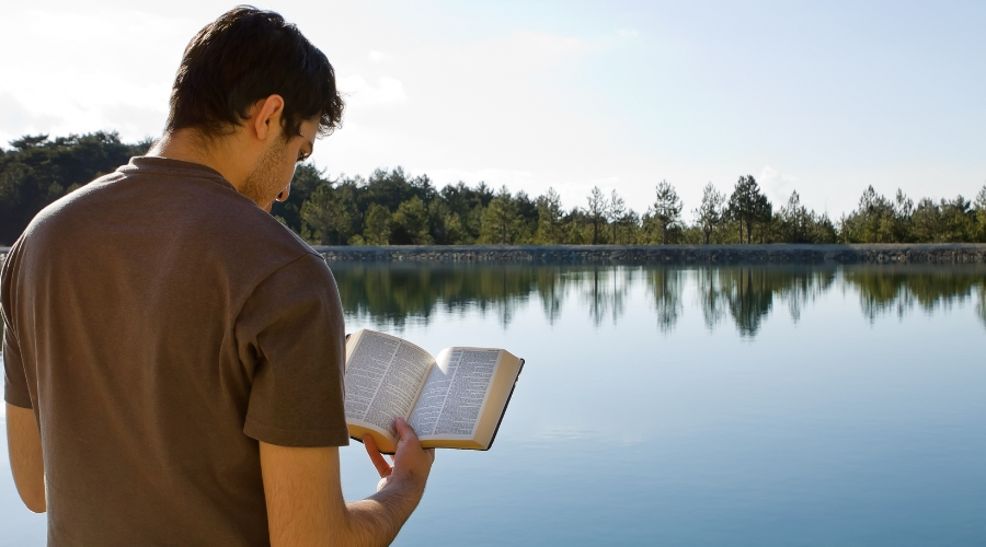 Water in the Bible - Man reading Bible near a lake of water